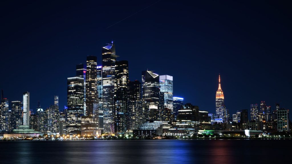 Relation transatlantique — vue nocturne captivante de la skyline de New York avec des gratte-ciel illuminés reflétant dans le fleuve Hudson