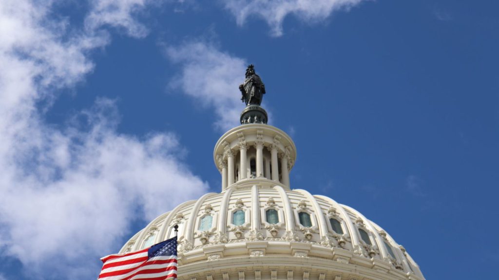 Interventions militaires américaines — capture du dôme du Capitole américain avec un drapeau américain flottant contre un ciel bleu à Washington, D.C
