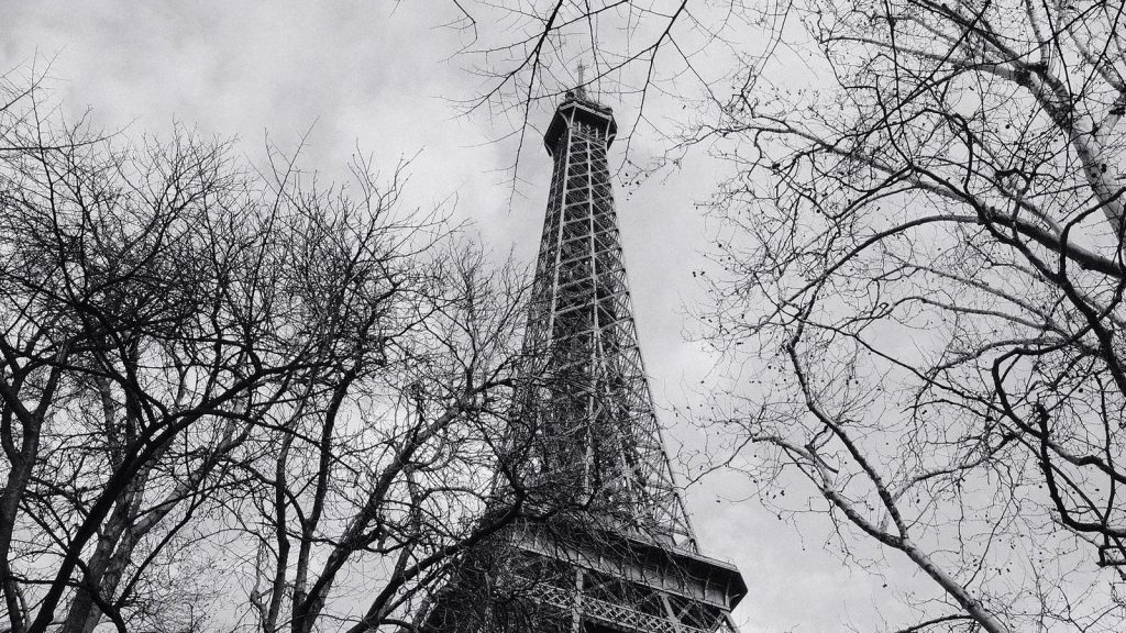 Photo en noir et blanc de la Tour Eiffel encadrée par des arbres dénudés par un jour nuageux.